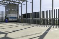 a blue and white bus is parked in front of a metal fence and a tall building