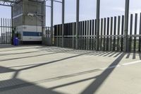 a blue and white bus is parked in front of a metal fence and a tall building