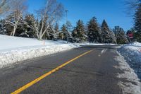 a yellow street sign sitting on the side of a road with snow on it under a blue sky