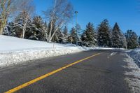 a yellow street sign sitting on the side of a road with snow on it under a blue sky