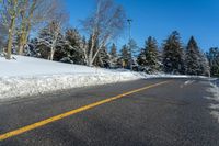 a yellow street sign sitting on the side of a road with snow on it under a blue sky