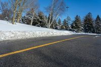 a yellow street sign sitting on the side of a road with snow on it under a blue sky