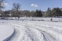 a road is covered with snow next to some trees and bushes near a fence on a field