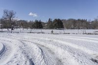 a road is covered with snow next to some trees and bushes near a fence on a field