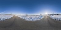 a wide angle shot of a road in the snow with a bright sun behind it