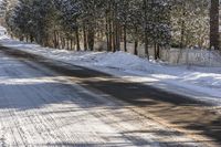 a street covered with snow in front of a tree lined area filled with trees, grass and snow