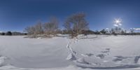 a snow covered field under a blue sky and clouds with a view looking down the hill