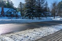 a house sits next to a street covered in snow and trees with sun shining on it