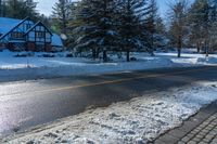 a house sits next to a street covered in snow and trees with sun shining on it