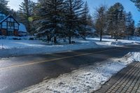 a house sits next to a street covered in snow and trees with sun shining on it