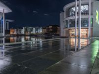 some buildings and buildings are reflected in the water at night while other buildings sit near a river