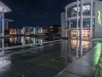 some buildings and buildings are reflected in the water at night while other buildings sit near a river