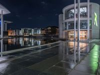 some buildings and buildings are reflected in the water at night while other buildings sit near a river