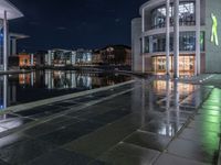 some buildings and buildings are reflected in the water at night while other buildings sit near a river