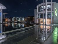 some buildings and buildings are reflected in the water at night while other buildings sit near a river