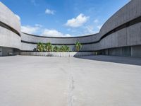 an empty parking lot with an open area in front of a large concrete building and palm trees