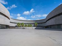 an empty parking lot with an open area in front of a large concrete building and palm trees