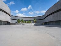 an empty parking lot with an open area in front of a large concrete building and palm trees