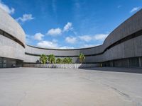 an empty parking lot with an open area in front of a large concrete building and palm trees