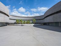 an empty parking lot with an open area in front of a large concrete building and palm trees