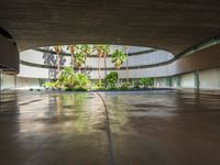 a large courtyard has concrete floors with trees and palm trees, a circular water feature and a low circular dome