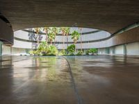 a large courtyard has concrete floors with trees and palm trees, a circular water feature and a low circular dome