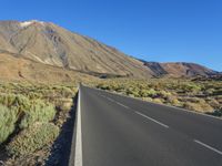 a paved empty highway leading to a large mountain range and a small blue sky above the valley