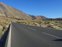 a paved empty highway leading to a large mountain range and a small blue sky above the valley