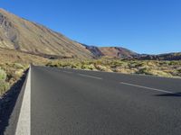 a paved empty highway leading to a large mountain range and a small blue sky above the valley