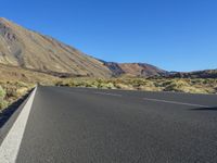 a paved empty highway leading to a large mountain range and a small blue sky above the valley