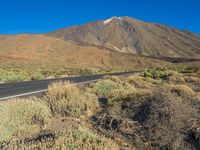 the mountains and road are seen with grass and scrub brush in the foreground and one is on a motorcycle