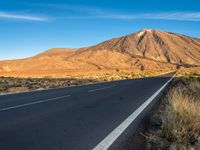 an empty road passes between a mountain and a desert area near a blue sky line