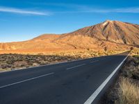 an empty road passes between a mountain and a desert area near a blue sky line