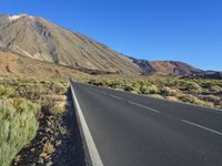 a long empty road with an outcropping on the side in front of mountains