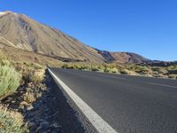 a long empty road with an outcropping on the side in front of mountains