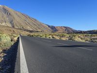 a long empty road with an outcropping on the side in front of mountains