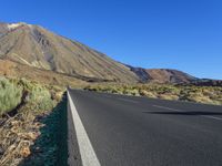 a long empty road with an outcropping on the side in front of mountains