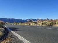 a bike lane in between two mountains and brush in the background, with a clear blue sky