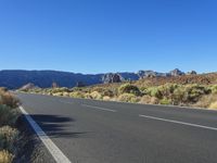 a bike lane in between two mountains and brush in the background, with a clear blue sky