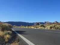 a bike lane in between two mountains and brush in the background, with a clear blue sky