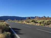 a bike lane in between two mountains and brush in the background, with a clear blue sky