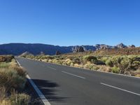 a bike lane in between two mountains and brush in the background, with a clear blue sky