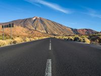 a paved road with mountain peaks in the background while sun shines below the horizon