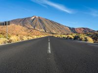 a paved road with mountain peaks in the background while sun shines below the horizon