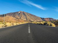 a paved road with mountain peaks in the background while sun shines below the horizon