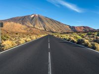 a paved road with mountain peaks in the background while sun shines below the horizon