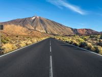 a paved road with mountain peaks in the background while sun shines below the horizon