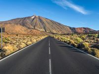 a paved road with mountain peaks in the background while sun shines below the horizon