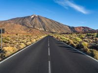 a paved road with mountain peaks in the background while sun shines below the horizon