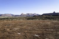 a barren field and mountain ranges, with a few snow patches in the dirt on the ground